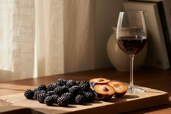 Rustic glass of deep purple blackberry-black-plum wine beside fresh blackberries and plums on walnut wood