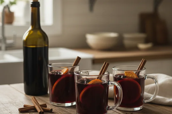 Warm cinnamon sticks beside a glass of deep amber wine on a walnut surface in soft natural light