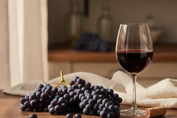 Clusters of deep-purple Concord grapes beside a glass of red wine on a walnut surface