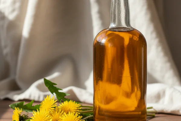 Bright dandelion blossoms beside a glass of golden wine on a walnut surface in soft natural light