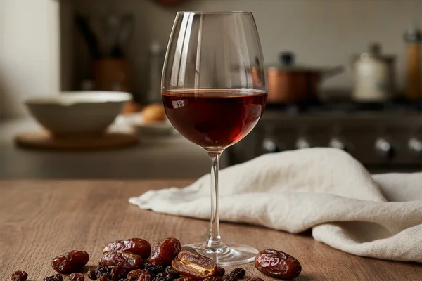Dried dates and raisins in a ceramic bowl on a walnut surface beside a glass of amber wine