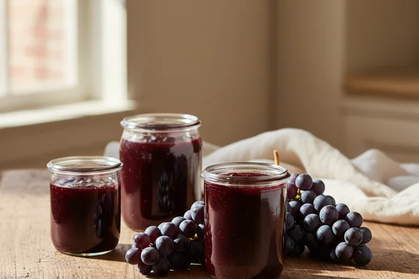 Dark grape concentrate in glass jars on a walnut surface beside winemaking equipment in soft natural light