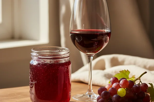 Jar of jewel-toned jelly wine on a walnut surface beside a glass of ruby liquid in soft natural light