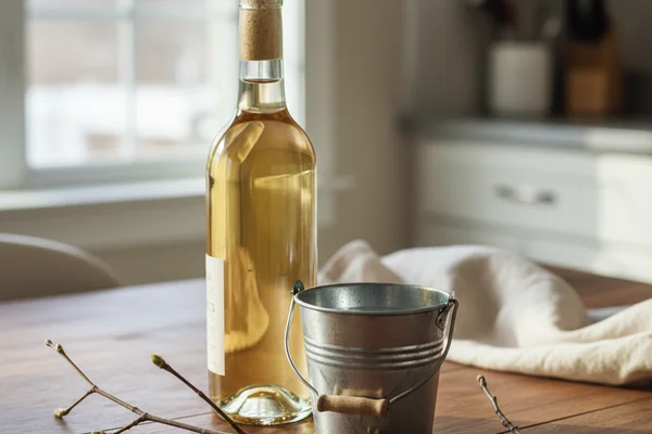 Pale golden maple sap wine in a glass beside a rustic jug on a warm walnut surface