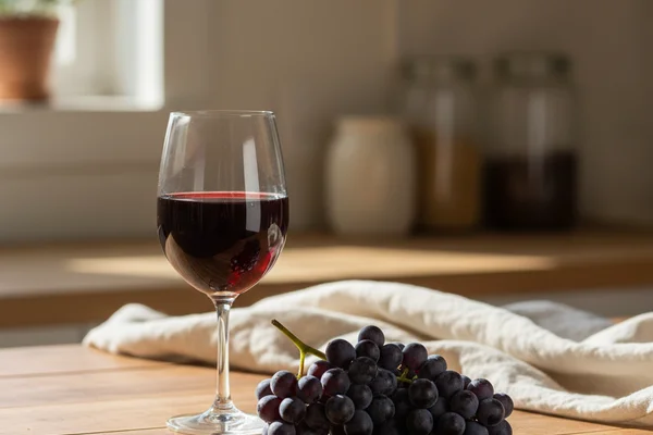 Deep red Mustang grape wine in a glass beside fresh wild grapes on a walnut surface in warm light