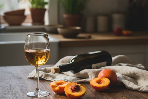 Ripe nectarines beside a glass of golden wine on a walnut surface in warm natural light