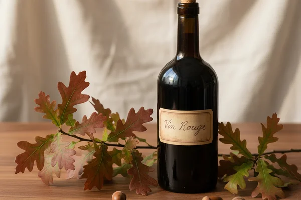 Fresh oak leaves beside a glass of pale golden wine on a walnut surface in warm natural light