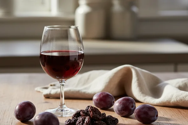 Rustic bowl of dried prunes on a walnut surface beside a glass of deep ruby wine in soft natural light