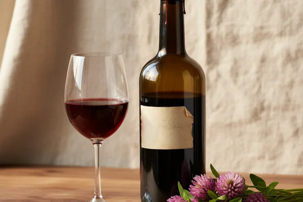 Fresh red clover blossoms beside a glass of pale rosé wine on a warm walnut surface