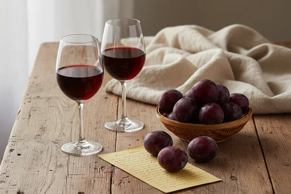 Wild plum wine fermenting in a glass carboy on a walnut surface beside fresh plums in soft natural light