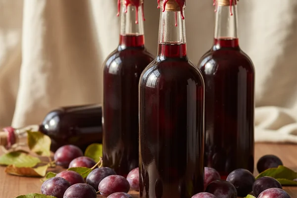 Wild plum wine in a glass bottle on a walnut surface, soft natural light, cream linen background