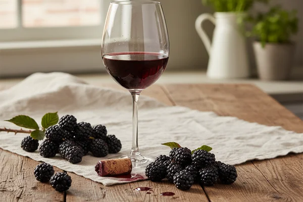 Brazos blackberry wine in a glass beside fresh blackberries on a walnut surface in warm natural light